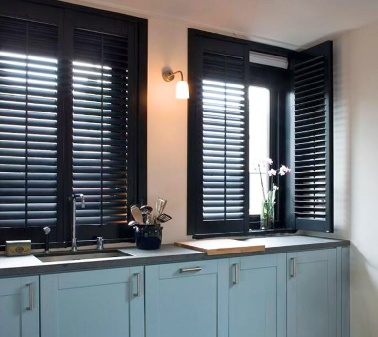 Modern kitchen with blue cabinets and large black-framed windows with shutters; sink and countertop visible.